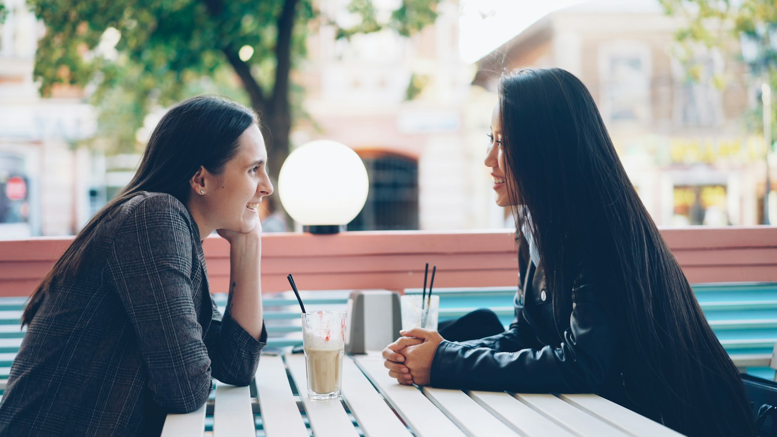 Two students sharing news over drinks at an open-air café